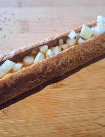 Echte foto van een frikandel speciaal; een frikandel met mayonaise, curry kruiden ketchup en ui. Geserveerd op een houten plank. De foto dient ter illustratie voor een artikel waar alle vragen over de frikandel worden beantwoord. Bijvoorbeeld: Waar is frikandel van gemaakt? En hoe lang is een frikandel?